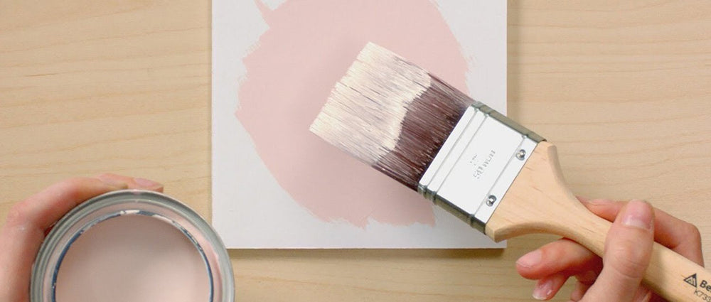 top down view of pink paint can with brush being held above white block with pink painted circle